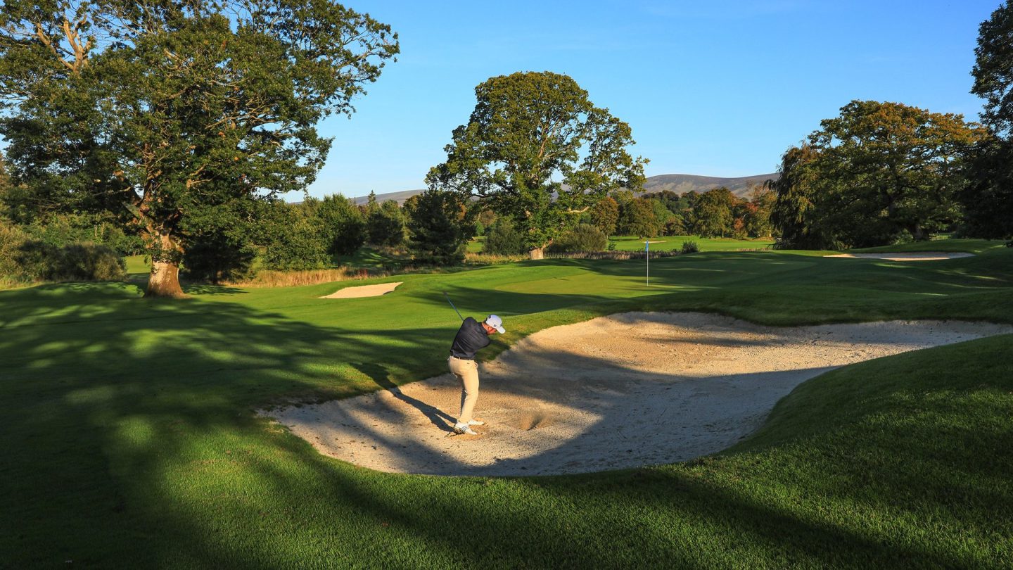 Gary Shaw playing a bunker shot towards a sunlit green.