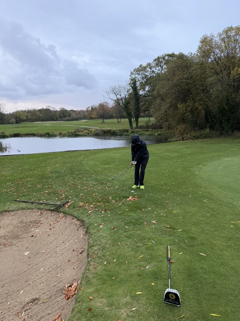 A golfer preparing a short shot beside a bunker at West Middlesex Golf Club.